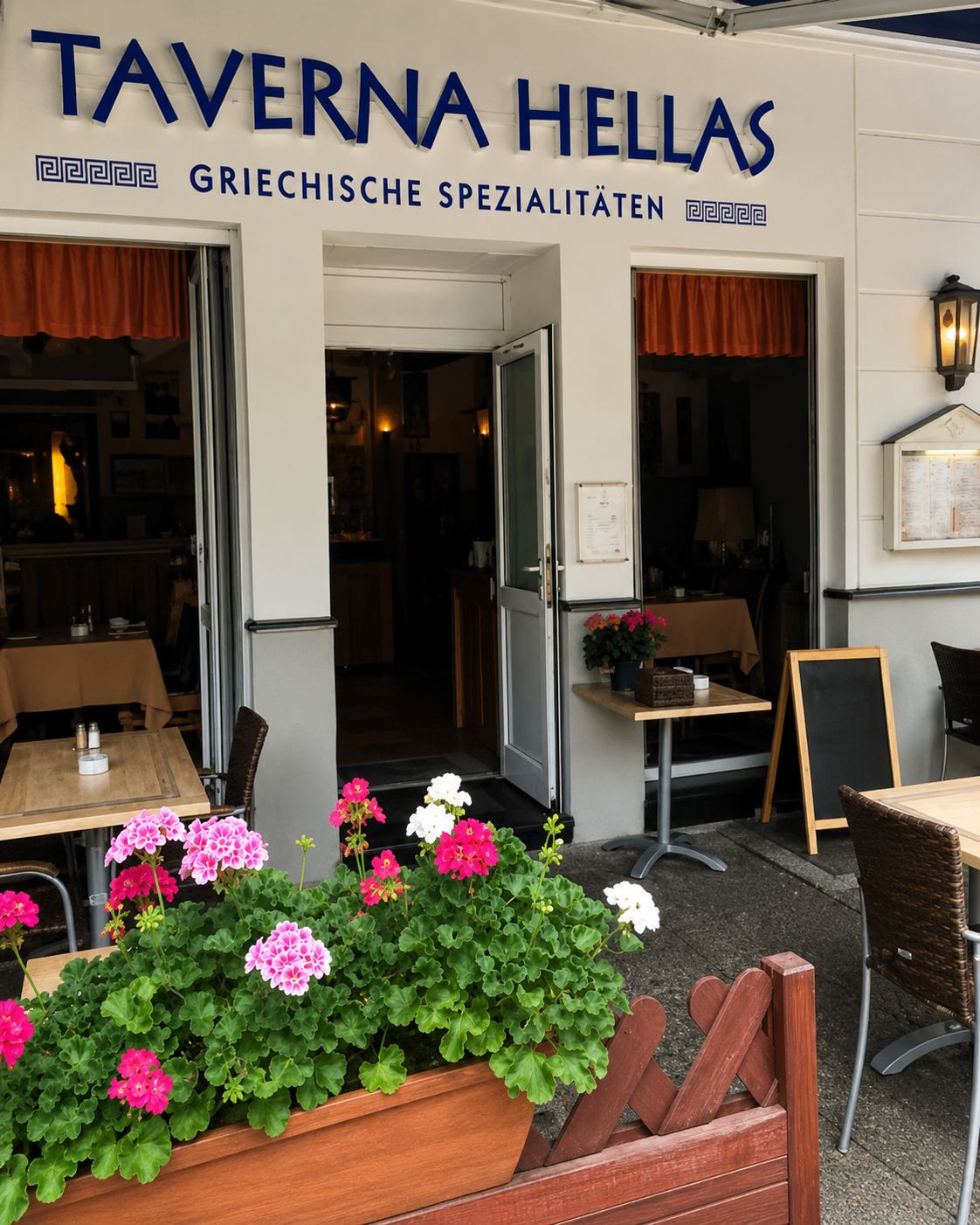 Der Eingang der Taverna Hellas mit Tischen im Freien und Blumenkästen.